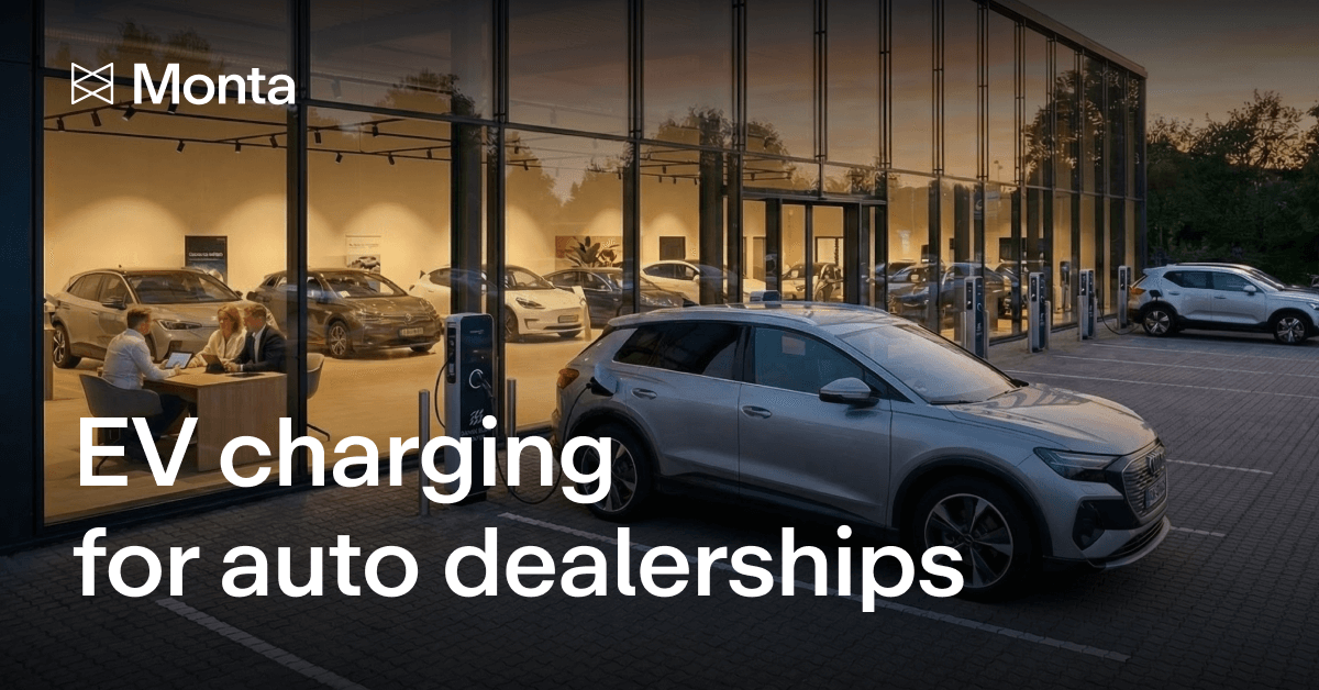 A modern auto dealership at dusk, featuring a white electric vehicle charging outside, with the interior showing several displayed cars.
