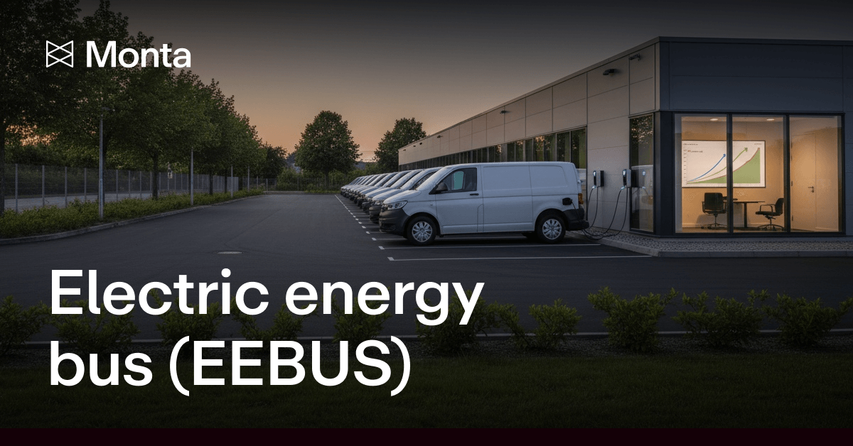 A row of electric vans charging in a modern facility, with a graph displayed on a screen in the background, under a twilight sky.