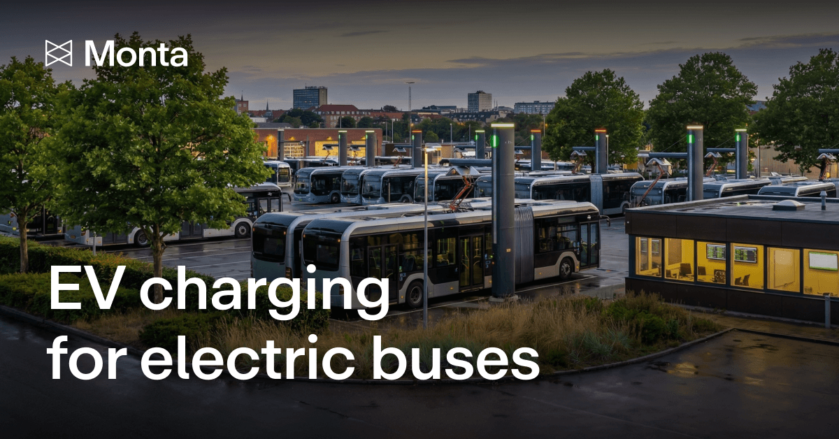 A fleet of electric buses charging at dusk, with illuminated charging stations and greenery surrounding a modern facility.