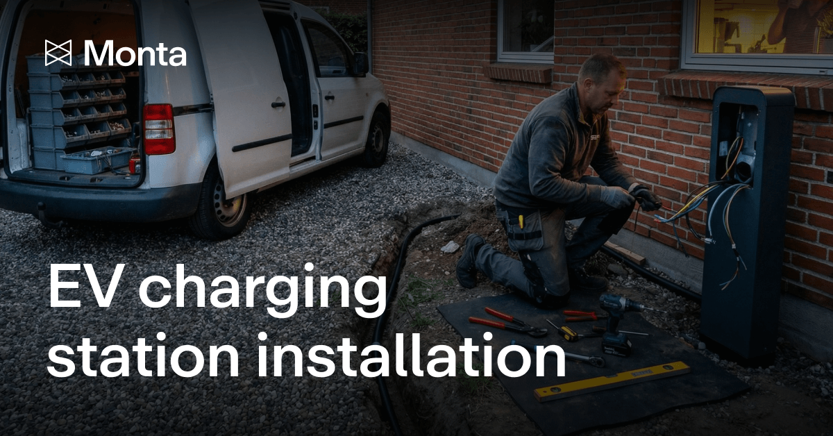 A technician installs an EV charging station by a wall, with tools and a white van nearby, set in a gravel area.