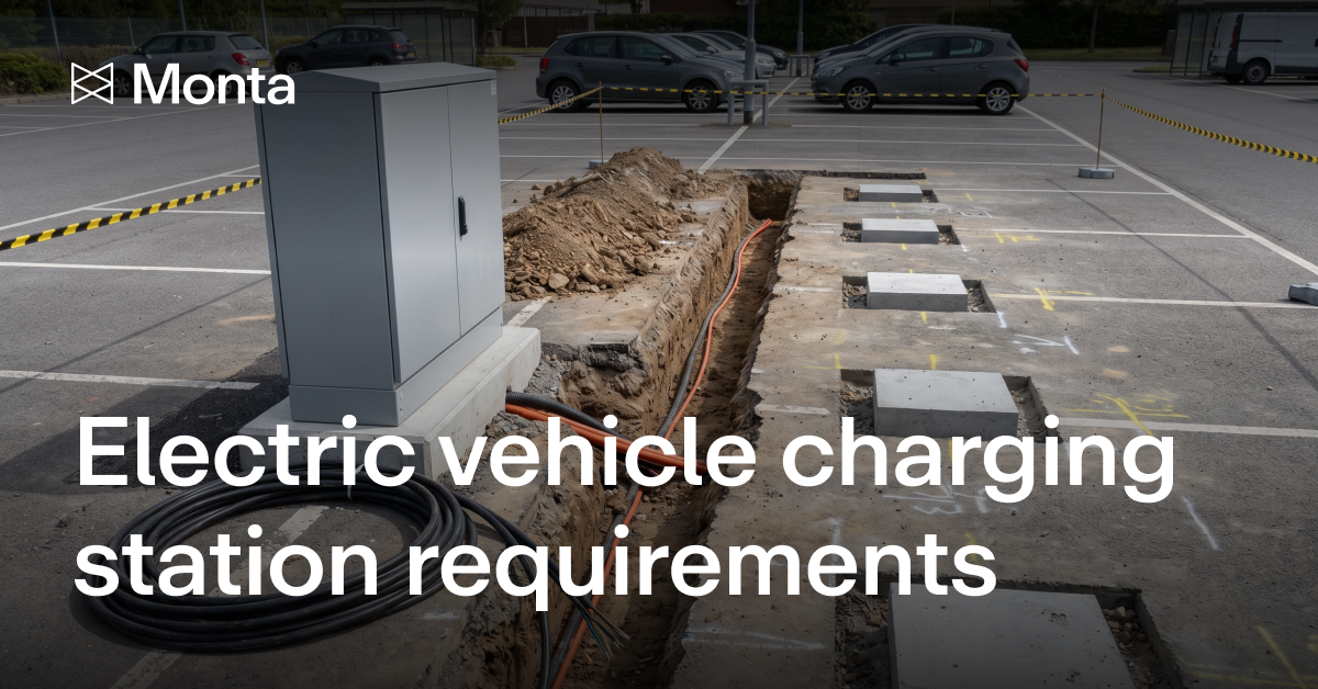 A trench dug across a car park with orange and black cables running through it, a coil of cable and a grey electrical cabinet beside it, and concrete charger foundations set into the tarmac.