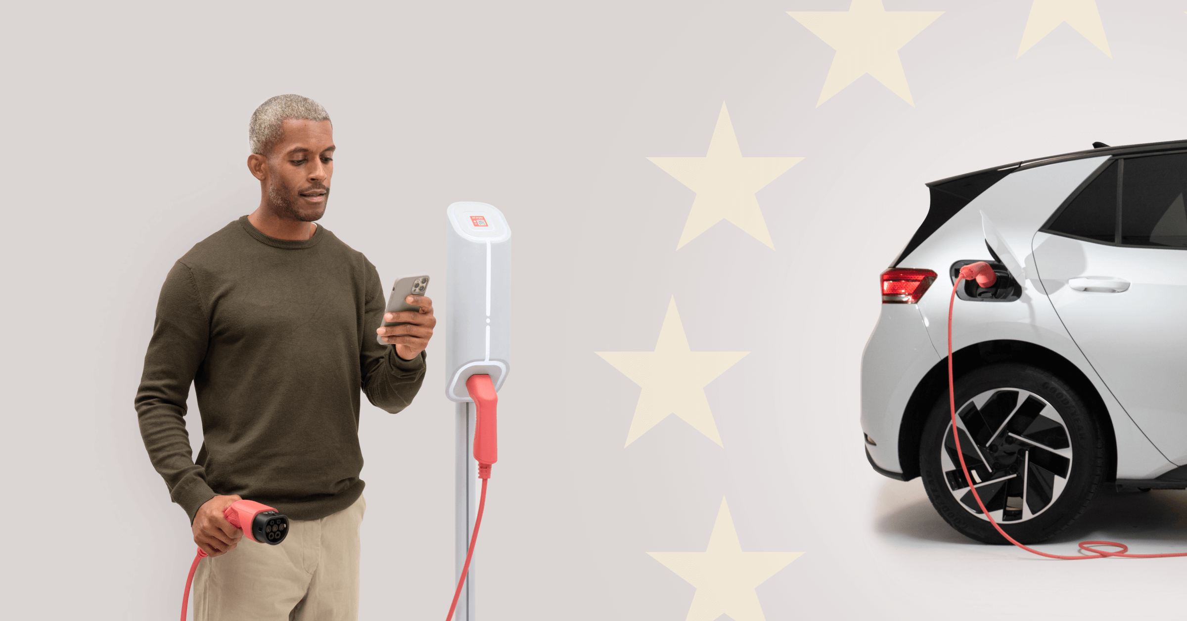 A man looks at his phone next to a charge point while a silver electric car charges, against a background of EU flag stars.