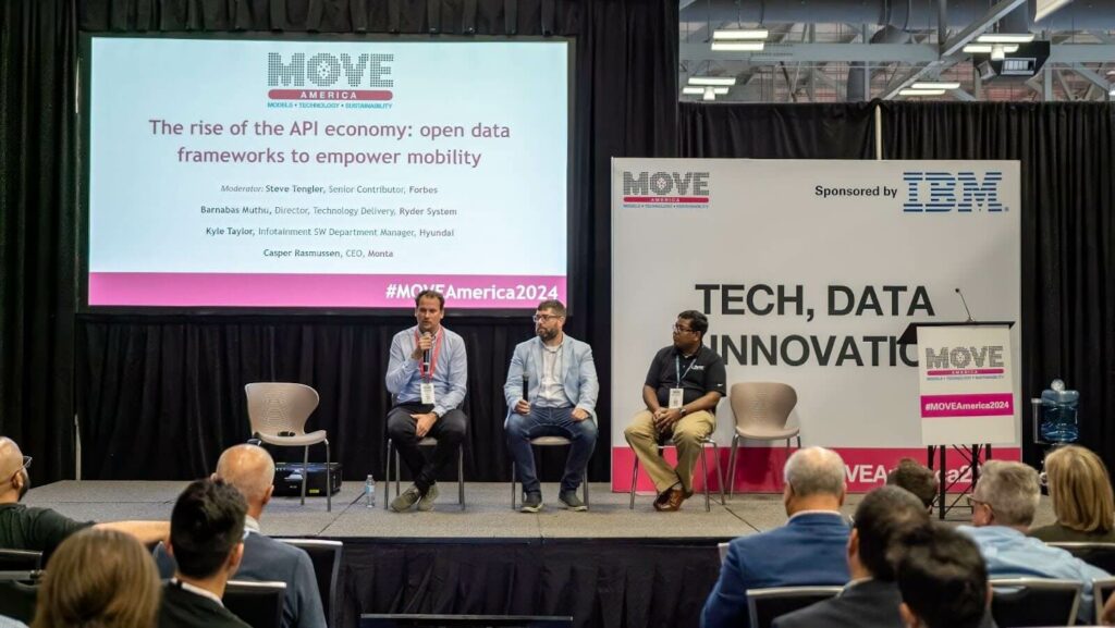 Three panellists seated on stage in front of a slide titled “The rise of the API economy: open data frameworks to empower mobility”, with an audience in the foreground