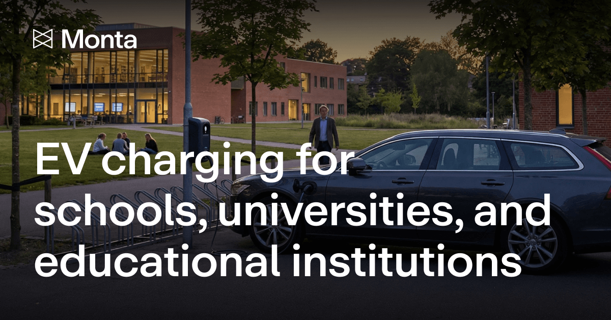A grey car parked by EV charging stations outside a brick building, with trees and a dusk sky in the background.