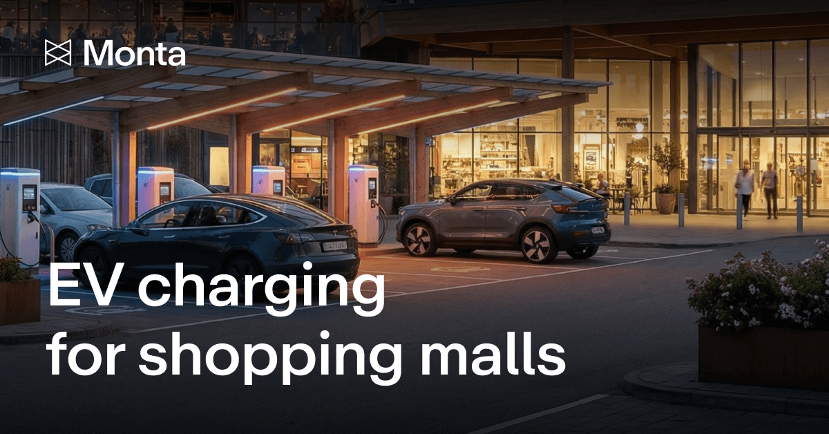 EV chargers with illuminated stations at a shopping mall, surrounded by parked cars and a stylish building in the background.