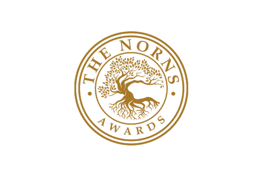 A circular emblem featuring a stylised tree with intricate roots and branches, surrounded by the text "THE NORNS AWARDS" in gold on a black background.